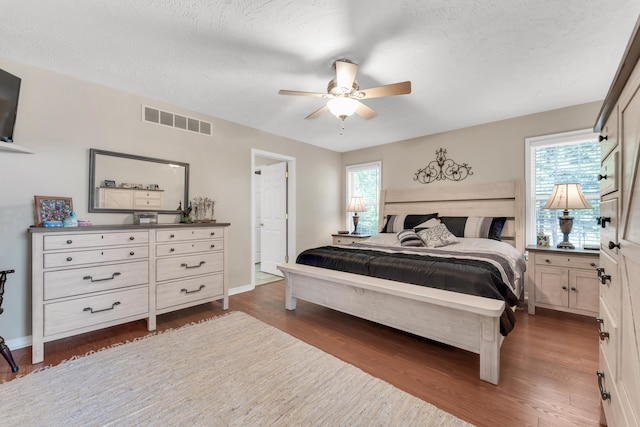 bedroom with ceiling fan, a textured ceiling, dark wood-type flooring, and multiple windows