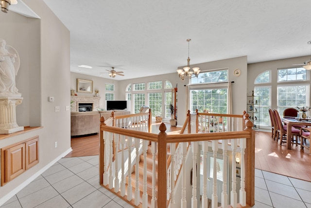 interior space featuring a brick fireplace, ceiling fan with notable chandelier, light wood-type flooring, and a textured ceiling