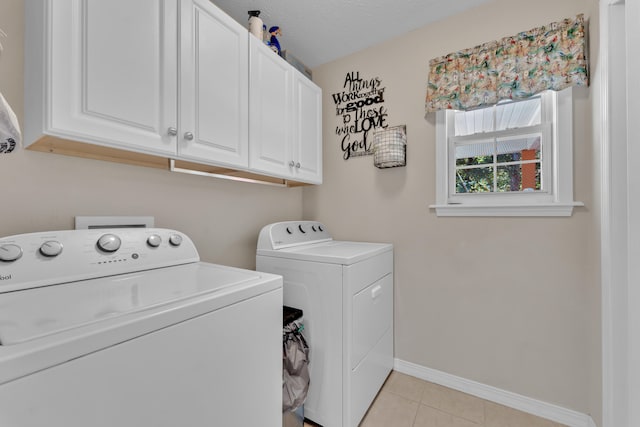 clothes washing area featuring a textured ceiling, washing machine and clothes dryer, light tile patterned floors, and cabinets