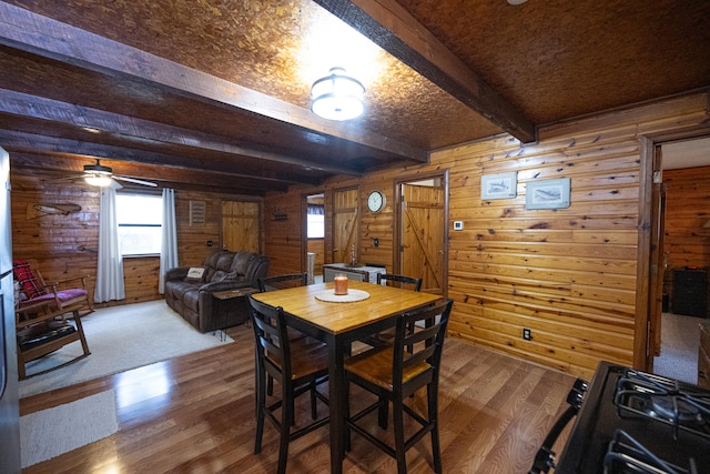 dining room featuring beam ceiling, hardwood / wood-style flooring, wooden walls, and ceiling fan