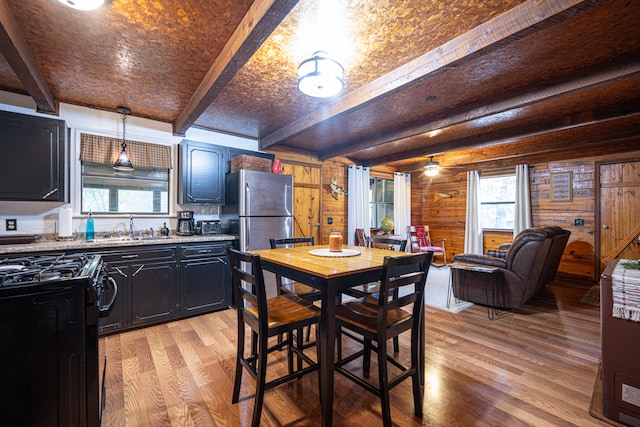 dining area featuring light wood-type flooring, beam ceiling, wood walls, and sink