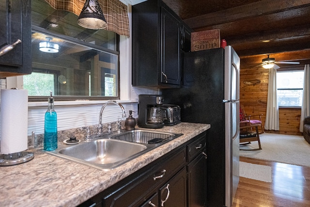 kitchen with wood walls, light hardwood / wood-style floors, stainless steel refrigerator, ceiling fan, and sink