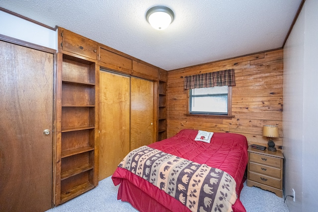 bedroom with a textured ceiling, wood walls, a closet, and light colored carpet