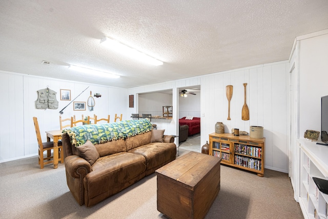 carpeted living room featuring ceiling fan, wooden walls, and a textured ceiling