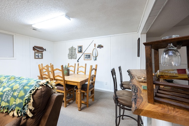 carpeted dining area with a textured ceiling and wooden walls