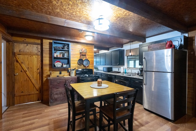 kitchen with gas stove, stainless steel refrigerator, wood walls, and light hardwood / wood-style floors