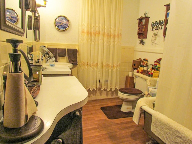 full bath with wood finished floors, a wainscoted wall, tile walls, and toilet