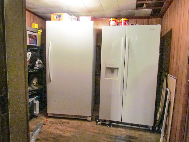 interior space with freestanding refrigerator, white refrigerator with ice dispenser, wood finished floors, brown cabinets, and wooden walls