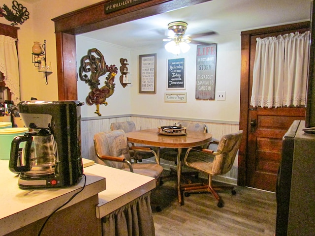 dining space featuring wood-type flooring, ornamental molding, ceiling fan, and wooden walls