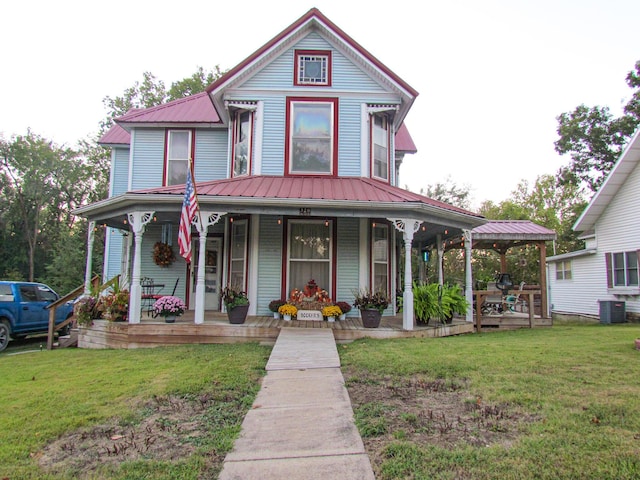 victorian home with covered porch, central AC unit, a front lawn, and metal roof