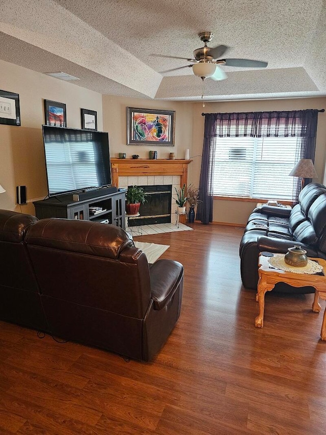 living room with a textured ceiling, ceiling fan, hardwood / wood-style floors, and a raised ceiling