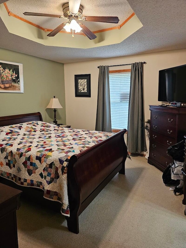 carpeted bedroom with a textured ceiling, ceiling fan, and a raised ceiling