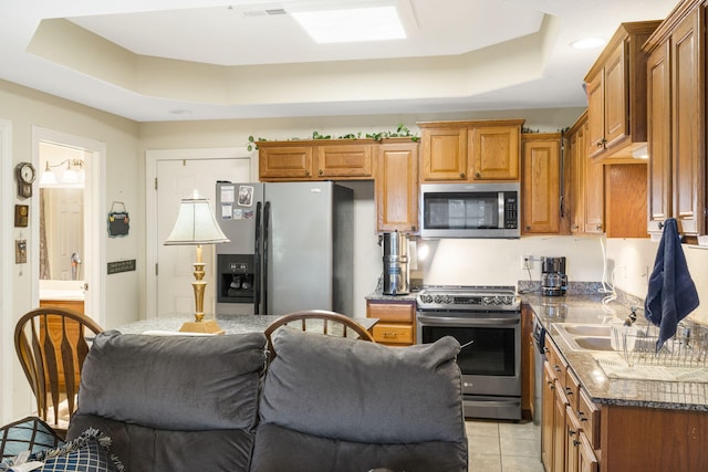 kitchen with light tile patterned floors, sink, stainless steel appliances, a tray ceiling, and dark stone countertops