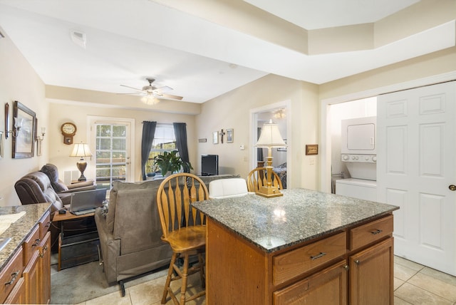 kitchen featuring stacked washing maching and dryer, ceiling fan, a kitchen island, a kitchen breakfast bar, and dark stone countertops