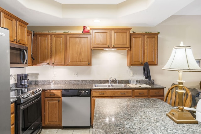 kitchen featuring dark stone countertops, a tray ceiling, appliances with stainless steel finishes, and sink