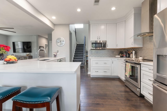 kitchen featuring sink, wall chimney exhaust hood, dark wood-type flooring, stainless steel appliances, and a kitchen breakfast bar