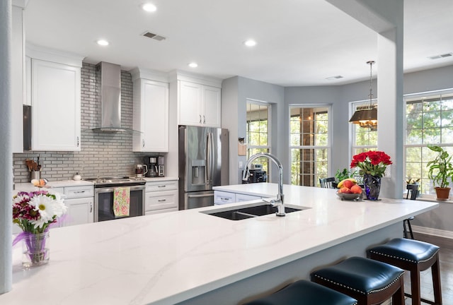 kitchen with a wealth of natural light, wall chimney range hood, sink, and stainless steel appliances