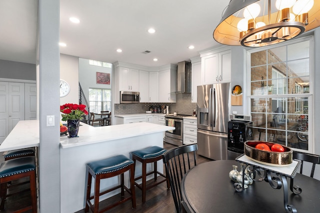 kitchen featuring wall chimney exhaust hood, kitchen peninsula, appliances with stainless steel finishes, and white cabinetry