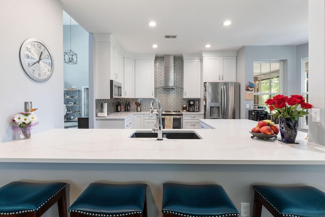 kitchen featuring kitchen peninsula, wall chimney range hood, stainless steel appliances, and a breakfast bar