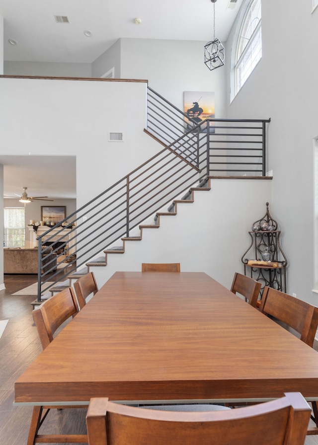 dining area featuring a high ceiling, wood-type flooring, and ceiling fan with notable chandelier