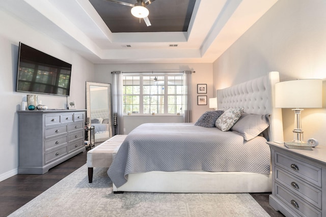 bedroom with ceiling fan, dark wood-type flooring, and a tray ceiling