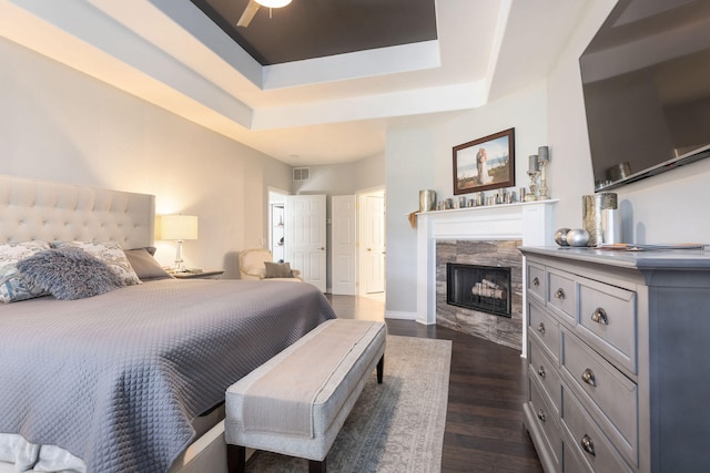 bedroom featuring a raised ceiling, ceiling fan, dark hardwood / wood-style flooring, and a tiled fireplace