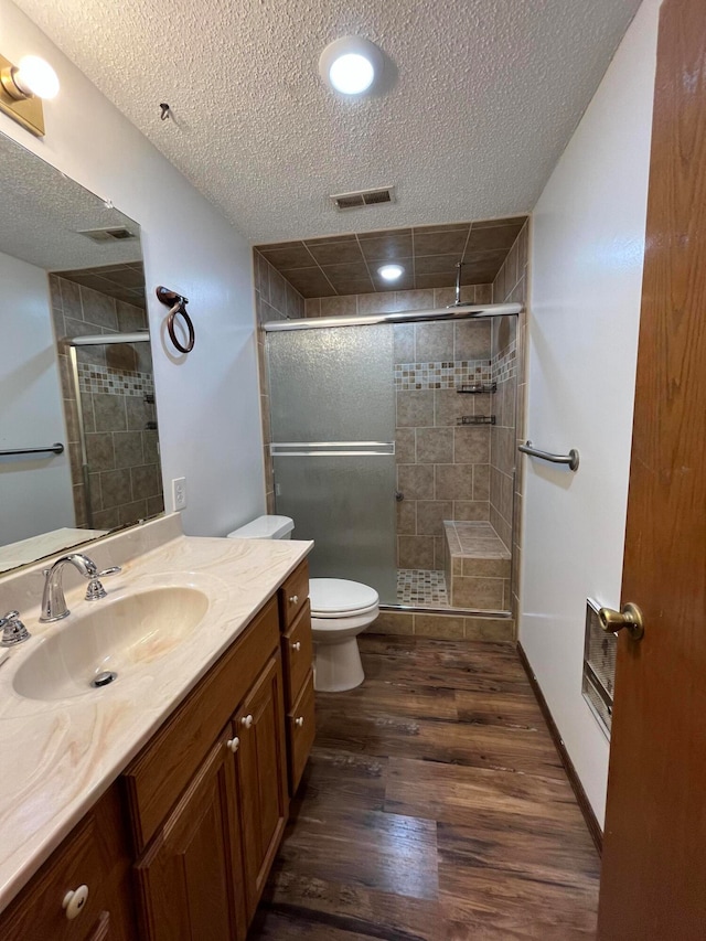 bathroom with a shower with door, a textured ceiling, wood-type flooring, toilet, and vanity