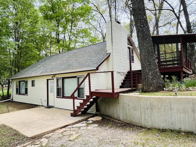 exterior space with a chimney, roof with shingles, stairway, and a deck