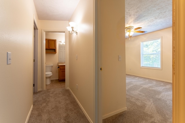 corridor with a textured ceiling and light carpet