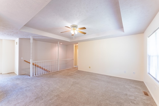 carpeted empty room with a textured ceiling, a raised ceiling, and ceiling fan