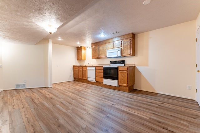 kitchen with light wood-type flooring, a textured ceiling, and white appliances