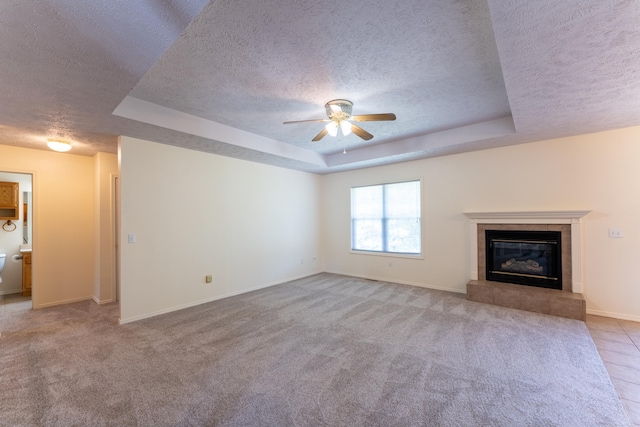 unfurnished living room featuring light carpet, a textured ceiling, a raised ceiling, and a tiled fireplace