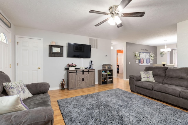 living room with ceiling fan with notable chandelier, light hardwood / wood-style floors, and a textured ceiling