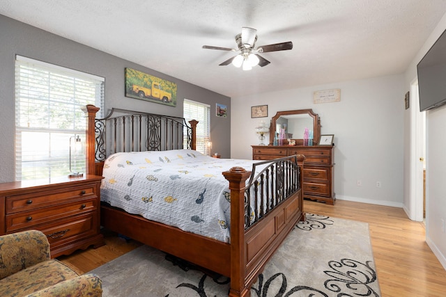 bedroom with a textured ceiling, ceiling fan, multiple windows, and light hardwood / wood-style flooring