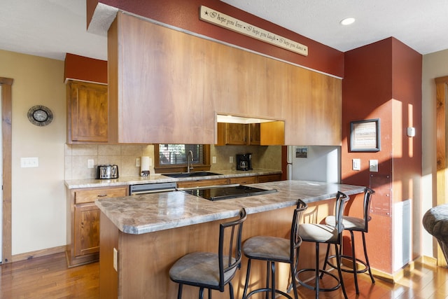 kitchen with sink, tasteful backsplash, a breakfast bar, black electric stovetop, and light wood-type flooring