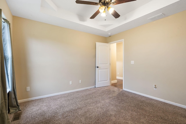 carpeted spare room featuring baseboards, a ceiling fan, visible vents, and a raised ceiling