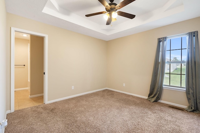 spare room featuring ceiling fan, a tray ceiling, light colored carpet, baseboards, and visible vents