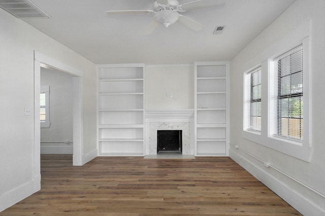 unfurnished living room featuring dark hardwood / wood-style floors, ceiling fan, a premium fireplace, and built in shelves