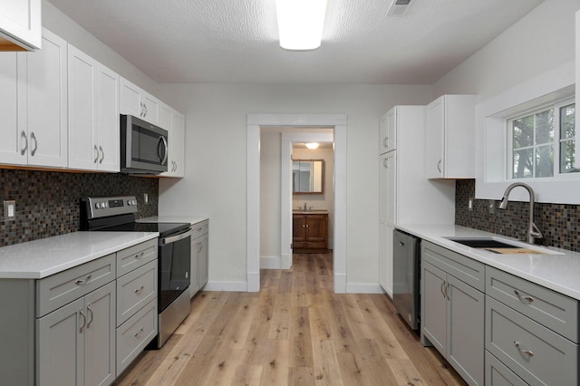 kitchen with sink, gray cabinetry, white cabinets, light hardwood / wood-style floors, and stainless steel appliances