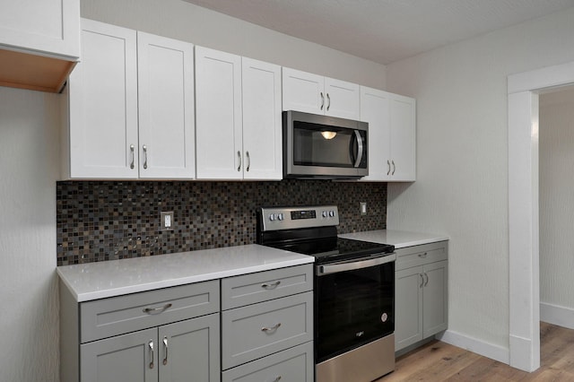 kitchen with gray cabinetry, light hardwood / wood-style flooring, appliances with stainless steel finishes, decorative backsplash, and white cabinets