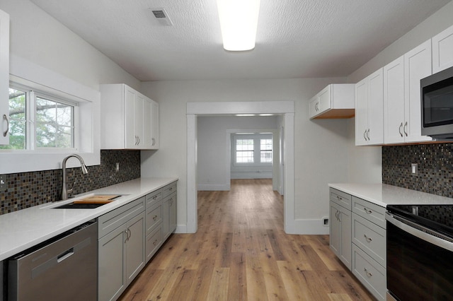 kitchen with sink, gray cabinetry, white cabinets, light hardwood / wood-style floors, and stainless steel appliances