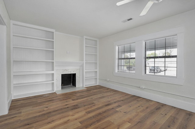 unfurnished living room featuring dark hardwood / wood-style floors, ceiling fan, a premium fireplace, and built in shelves