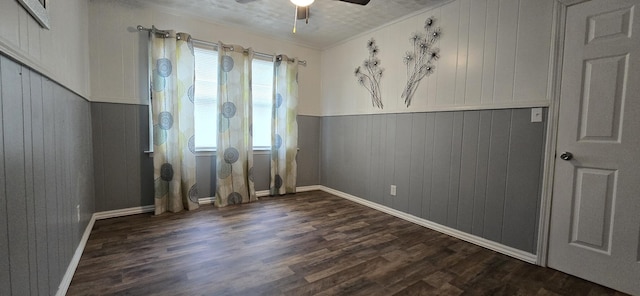empty room with ceiling fan, crown molding, dark wood-style flooring, wood walls, and baseboards