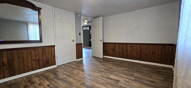 empty room with wainscoting, wood finished floors, wood walls, and a textured wall