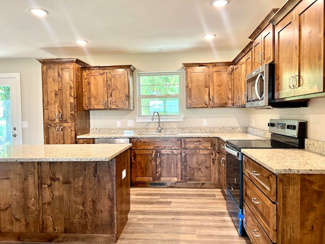 kitchen featuring light stone counters, appliances with stainless steel finishes, light wood-type flooring, and sink