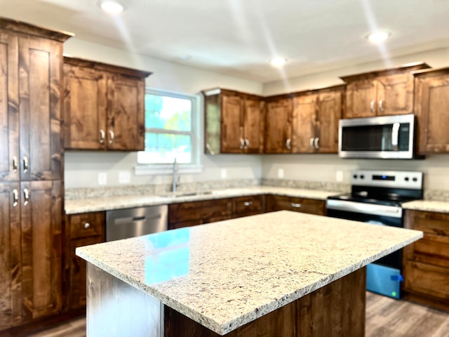 kitchen with light wood-type flooring, a kitchen island, sink, stainless steel appliances, and light stone countertops