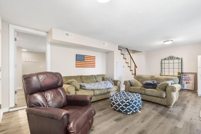 living room with light wood-type flooring, stairs, baseboards, and visible vents