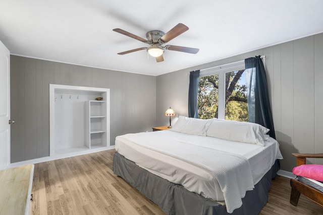 bedroom with light wood-style floors, a decorative wall, and a ceiling fan