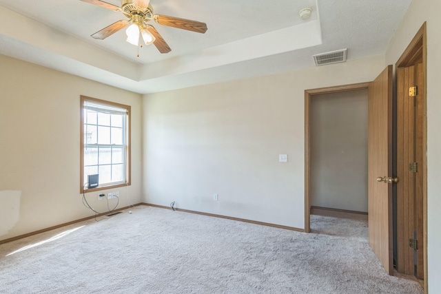 empty room featuring a textured ceiling, light colored carpet, ceiling fan, and a raised ceiling