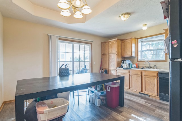 kitchen with hardwood / wood-style floors, sink, a tray ceiling, black dishwasher, and an inviting chandelier